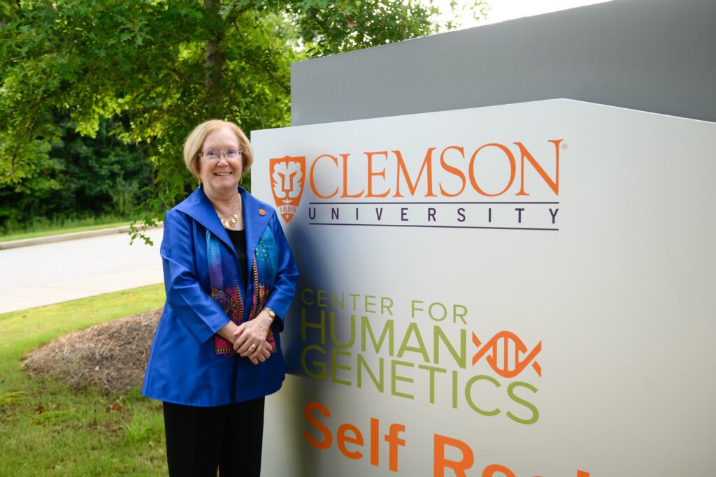 A woman in a blue suit stands next to the Clemson University Center for Human Genetics sign.