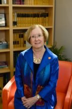 a woman in a blue suit sits on an orange chair in front of some bookshelves